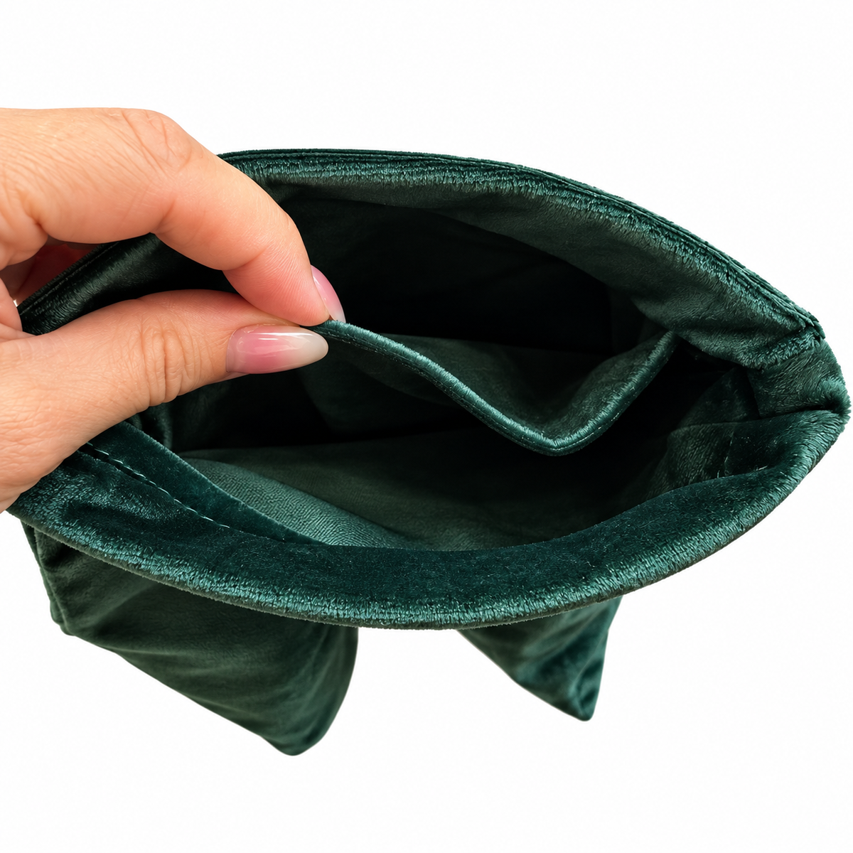 A close-up of a dark green velvet rack bag being held open by a hand, showing the plush texture of the exterior and lining against a white background.