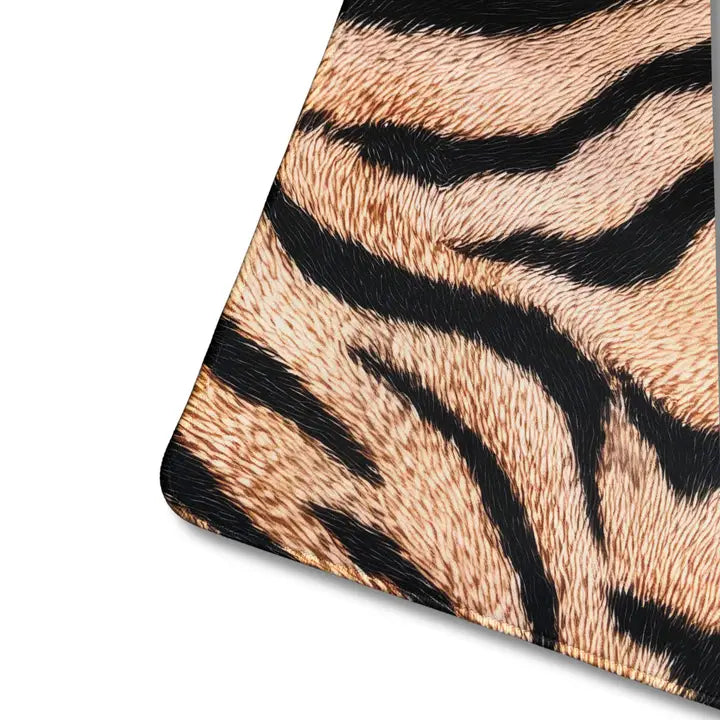 A close-up of a tiger-print material swatch showing black stripes over a warm tan and cream furry texture, cropped diagonally on a white background.